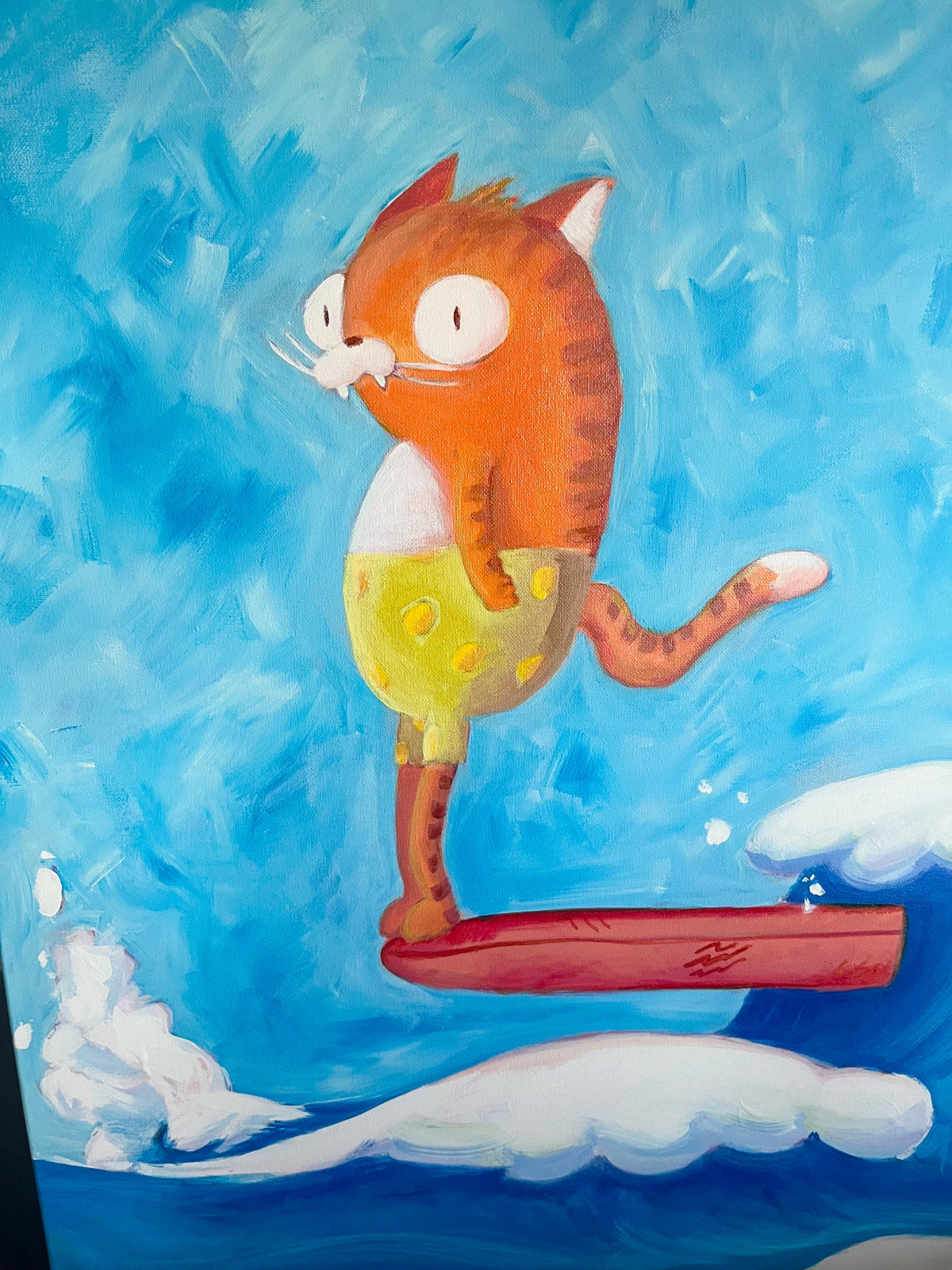 A colorful painting of an orange tabby cat wearing yellow shorts with white polka dots, balancing on a red surfboard against a textured blue sky and ocean background.