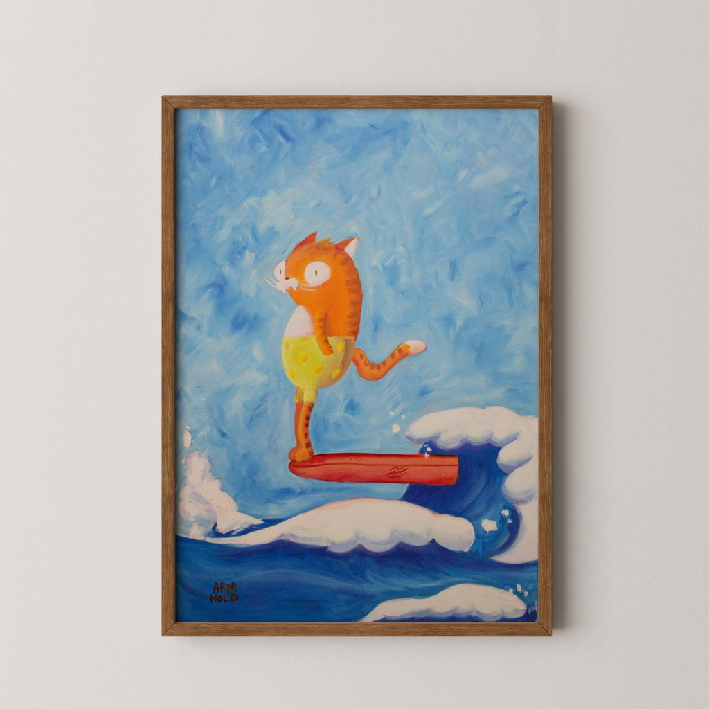 A framed art print featuring a whimsical illustration of an orange cat surfing on a wave, mounted on a light beige wall.
