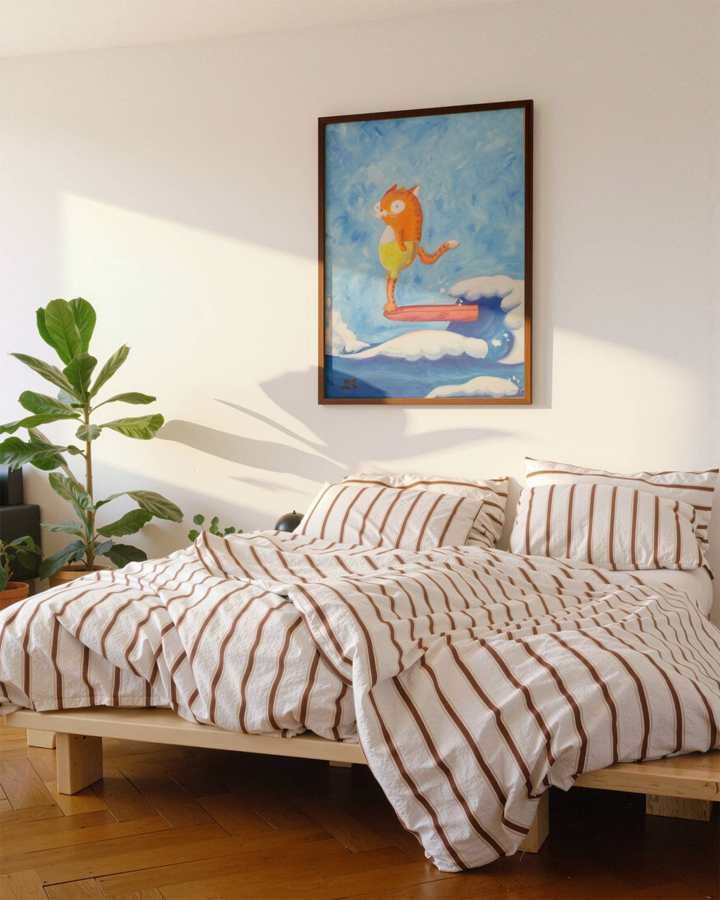 A styled bedroom scene featuring a bed with cream and brown striped bedding, set against a white wall with a framed colorful painting hanging above. A green potted plant is visible on the left, and warm sunlight casts shadows across the wall and bedding.