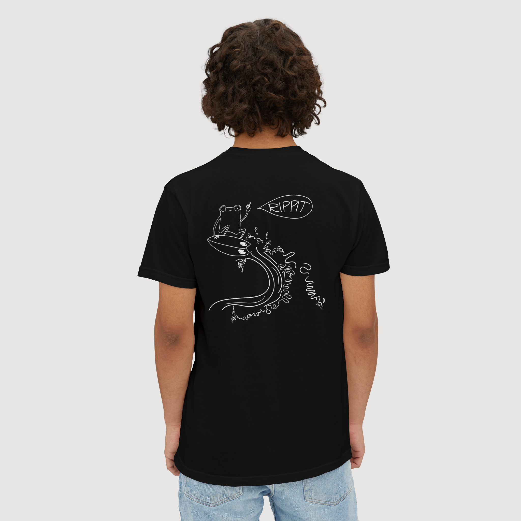 back view of a male model wearing a black surfjoy t-shirt featuring a design of a frog catching an air on a wave with a speech bubble that says 'rippit'