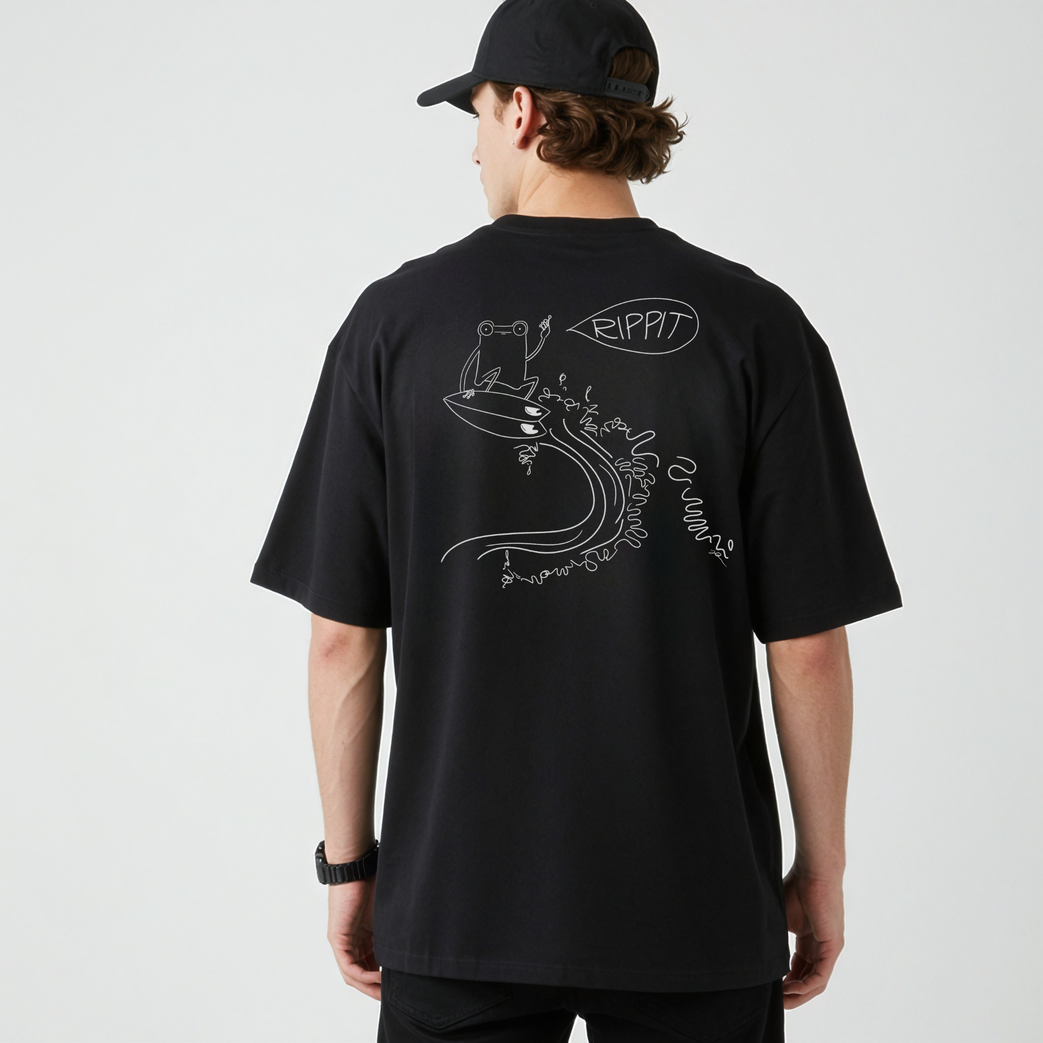 male model in a hat wearing a black surfjoy t-shirt featuring a design of a frog catching an air on a wave with a speech bubble that says 'rippit'
