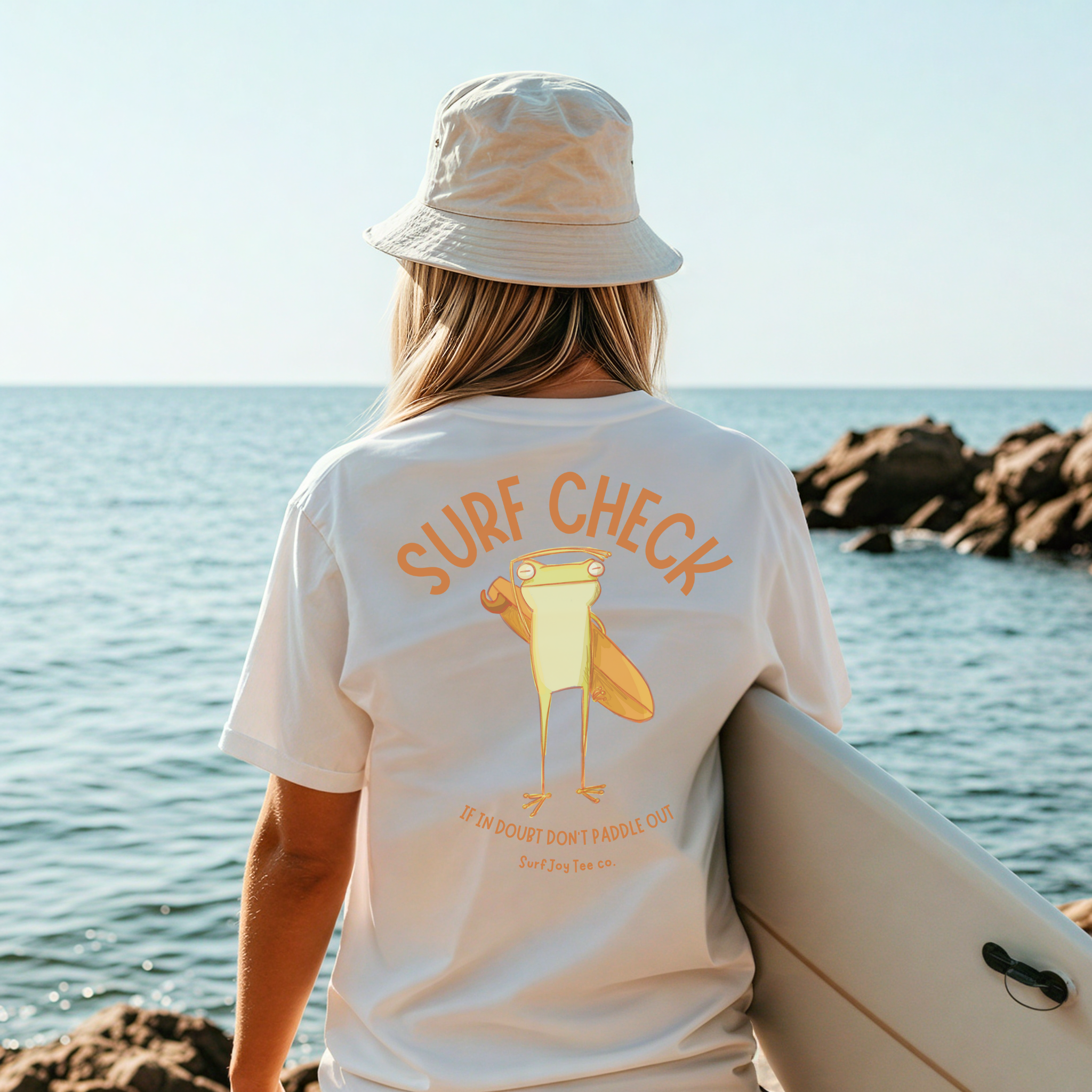 surfer woman wearing a surfjoy t-shirt featuring a funny design of a frog checking the surf conditions next to text that says 'if in doubt, don't paddle out'