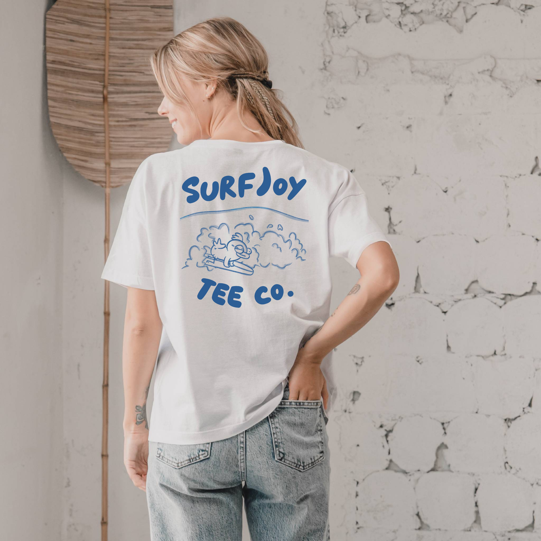 woman wearing a funny surfer t-shirt with a surfing chicken design next to text that says 'surfjoy tee co.'