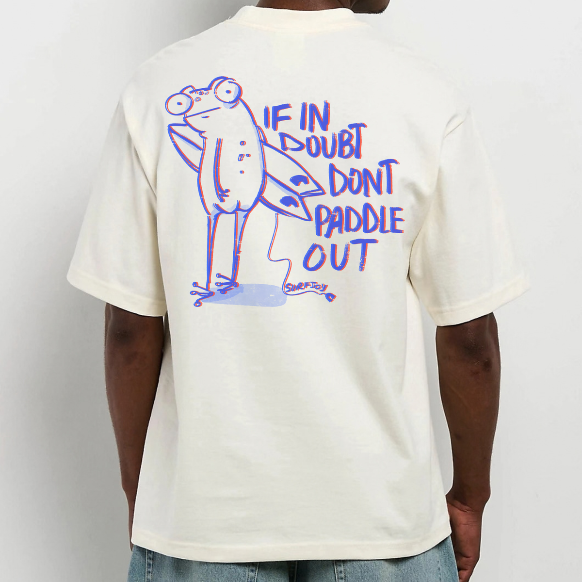 Male model wearing an oversized T-shirt with humorous graphic of frog character with surfboard and quote "If in doubt don't paddle out" printed on the back
