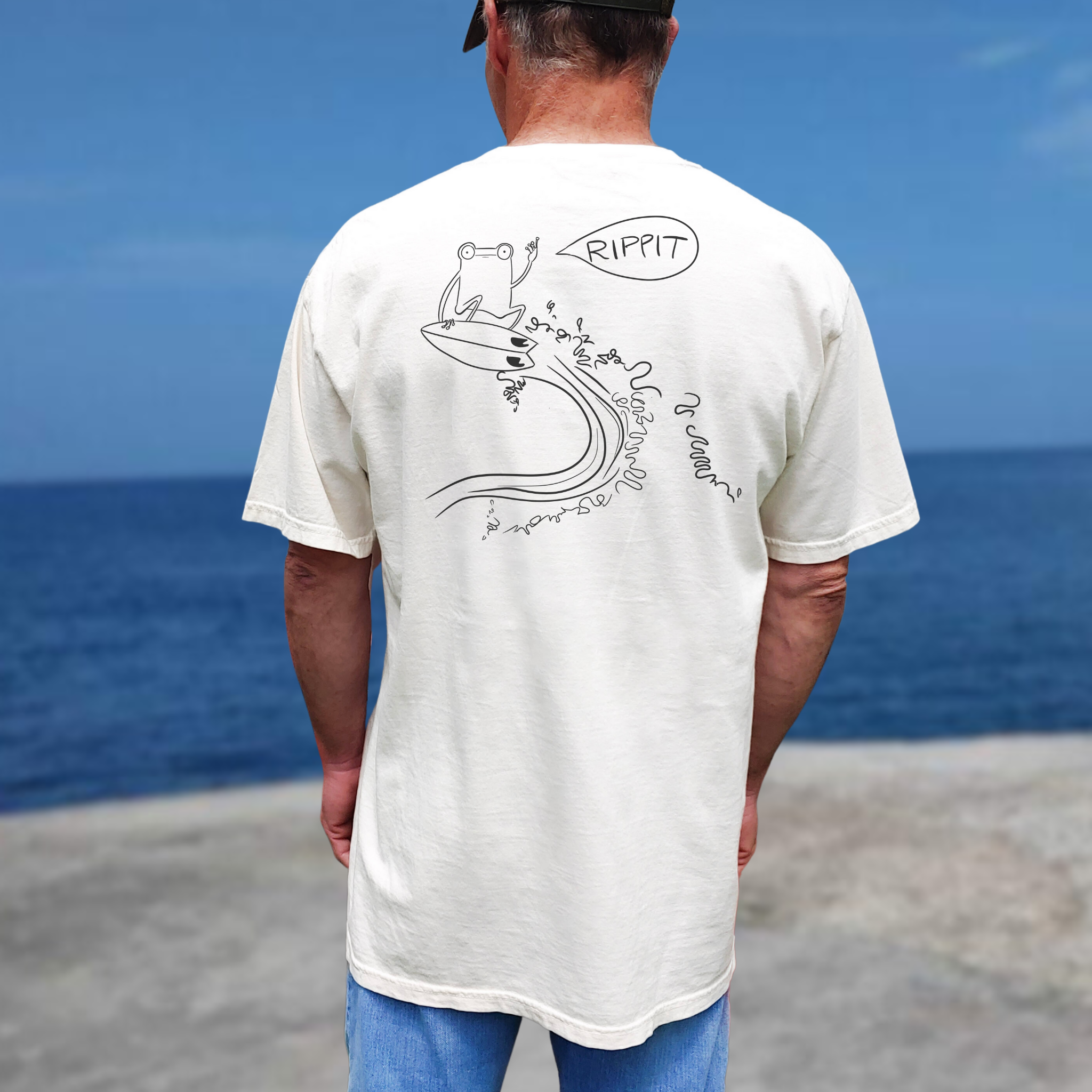 man near the ocean wearing the surfjoy original rippit t-shirt with a design of a frog catching air on a wave