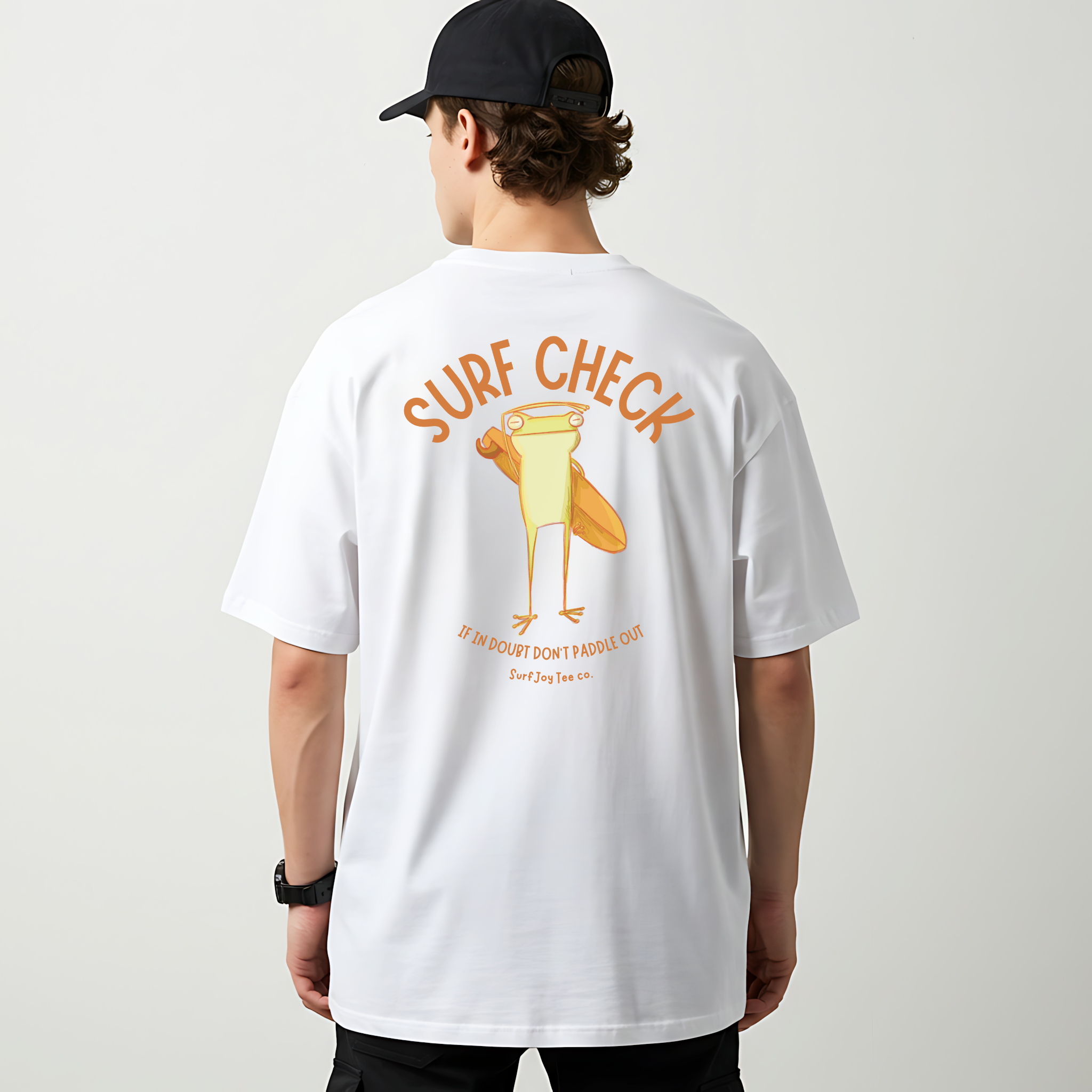male model wearing a white surfjoy t-shirt featuring a funny design of a frog checking the surf conditions next to text that says 'if in doubt, don't paddle out'