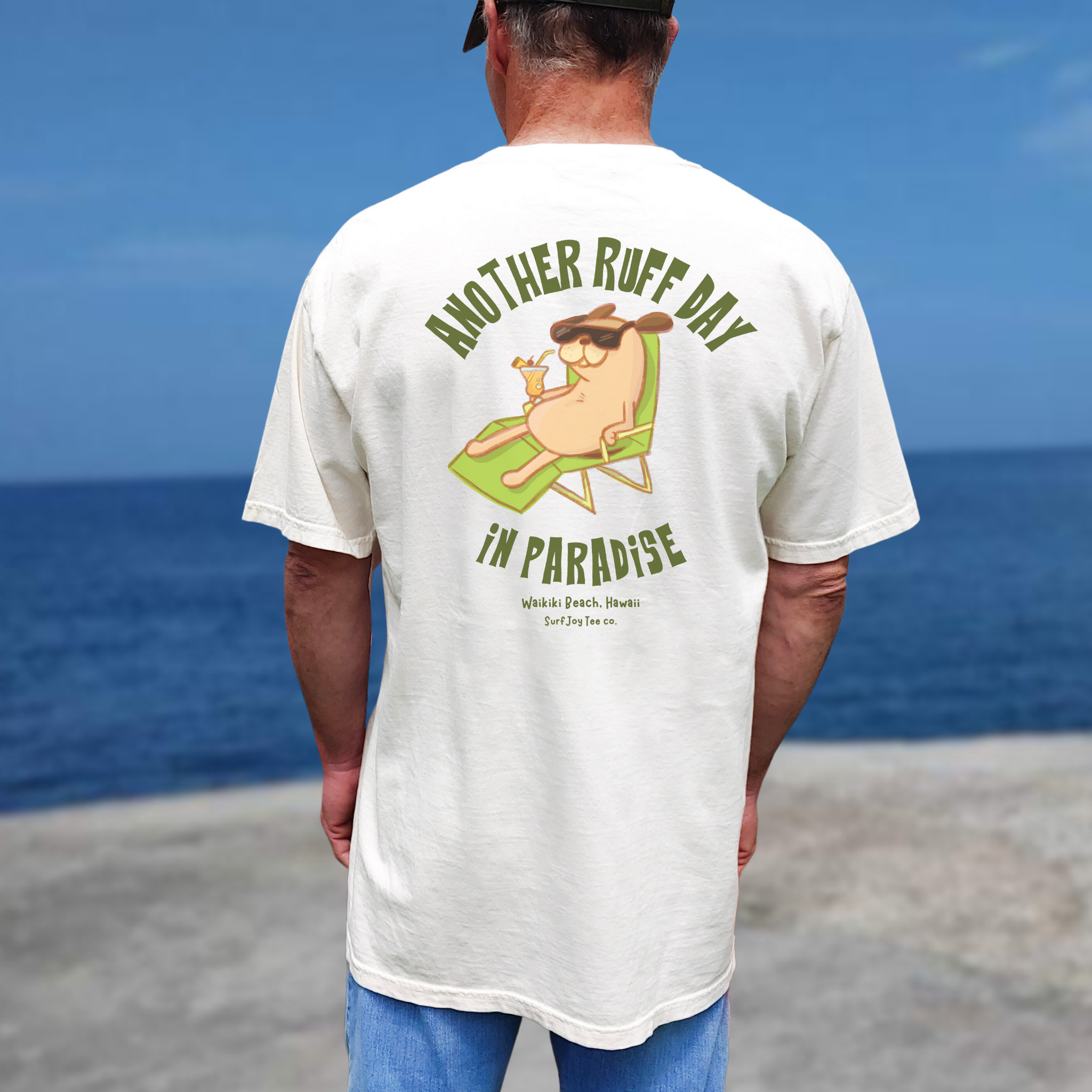 person wearing a waikiki beach t-shirt featuring a dog in a beach chair with text thats says 'another ruff day in paradise' on the beach
