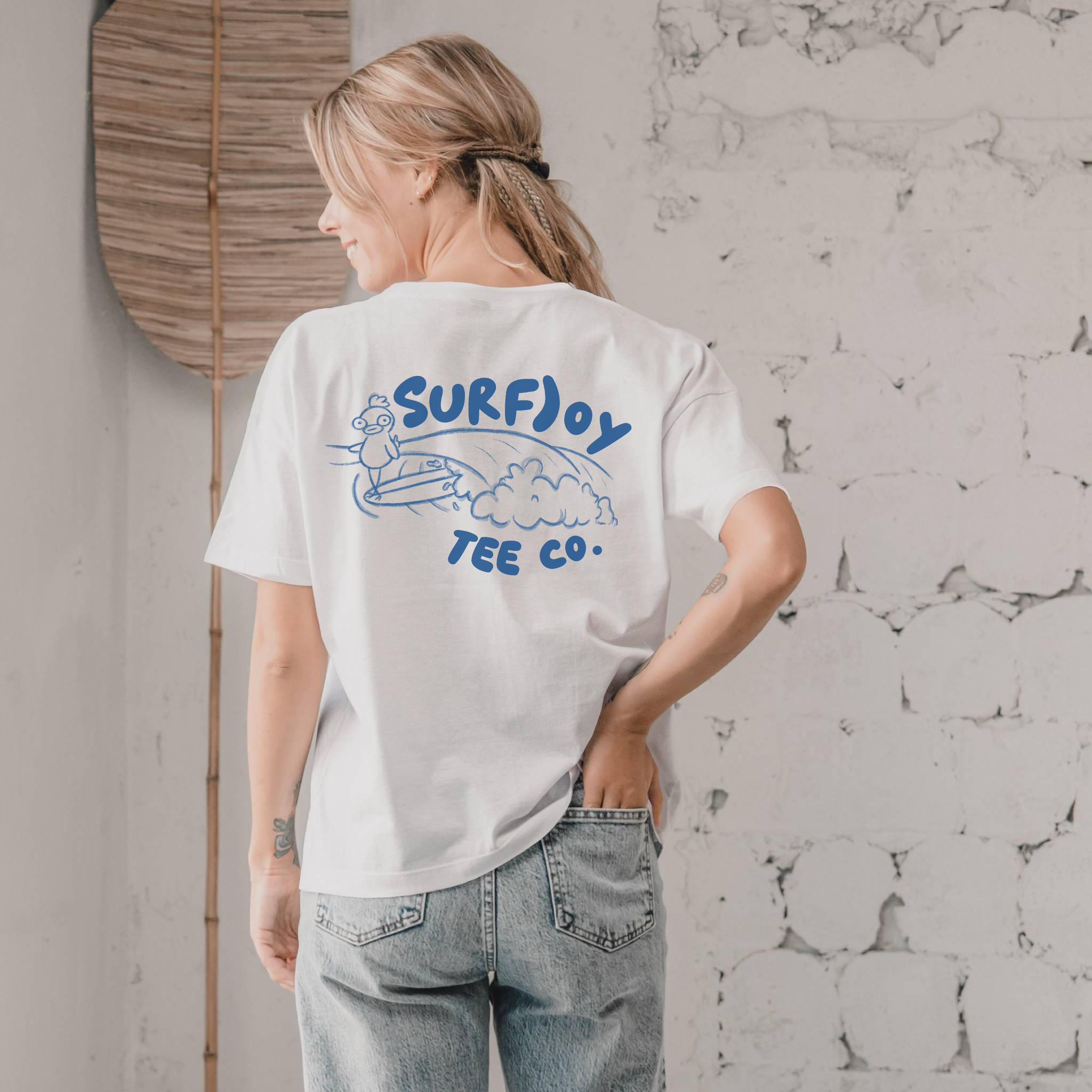 woman wearing a surf t-shirt with funny design of a surfing chicken by text that says 'surfjoy tee co.'